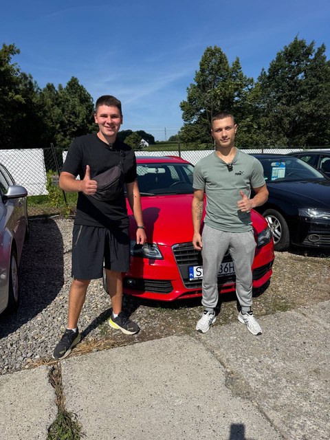 Dwóch klientów przy czerwonym hatchbacku na placu