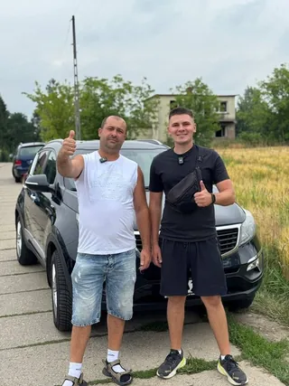 Двоє клієнтів біля темного авто, за майданчиком поле