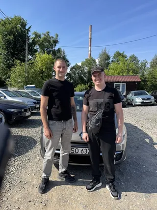 Двоє клієнтів біля темного авто на гравійному майданчику